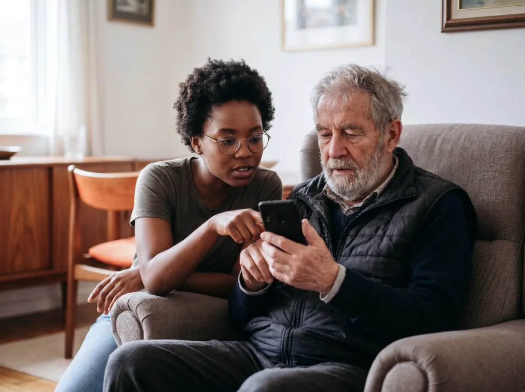 A younger family member helping an older man use his phone at home