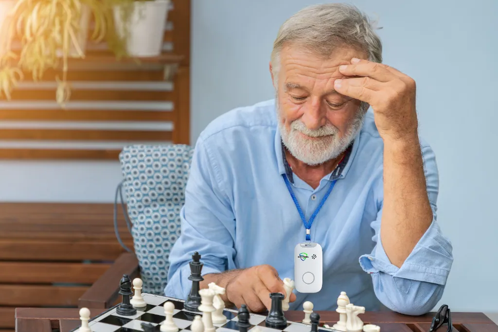 An older man playing chess at home while wearing a Sentinel pendant